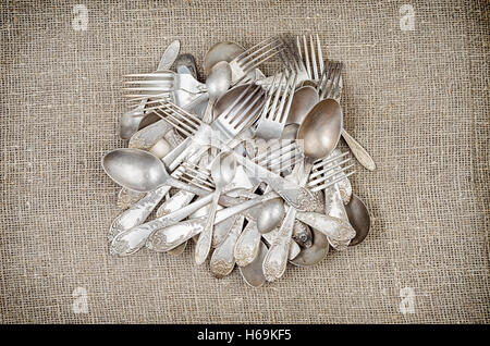 Pile of aged vintage silver cutlery (fork, knife, spoons) on rustic jute background. Stock Photo