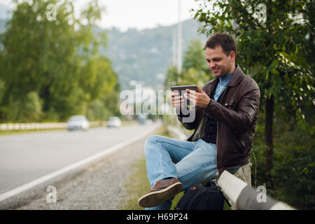 Man sitting on a road fence with gps tablet pc and using online maps Stock Photo