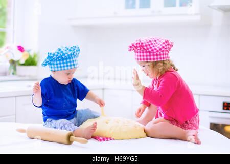 Cute kids, adorable little girl and blond curly boy making dough for a cake. Children mix flour, eggs and milk baking apple pie Stock Photo