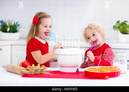 Cute kids, adorable little girl and blond curly boy making dough for a cake. Children mix flour, eggs and milk baking apple pie Stock Photo