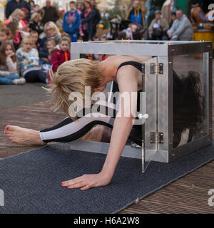 Circus contortionists squeeze into a small glass Cube at Southport. A contortionist woman enters & exits (Enterology) into a small, knee-high cube box. Performing flexible female contortionists show an insane stretching routine as the cabaret show entertains the audience at Pleasureland,  Merseyside UK. Stock Photo