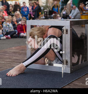 Circus contortionists squeeze into a small glass Cube at Southport. A contortionist woman enters & exits (Enterology) into a small, knee-high cube box. Performing flexible female contortionists show an insane stretching routine as the cabaret show entertains the audience at Pleasureland,  Merseyside UK. Stock Photo