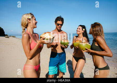 Portrait of young man and women drinking fresh coconut water by the sea. Group of young friends having fun on summer beach vacat Stock Photo