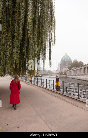 woman in red coat under weeping willow near river spree and berliner dom in berlin Stock Photo