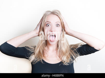 Young beautiful blond woman astonished stunned portrait, hands on head and open mouth Stock Photo