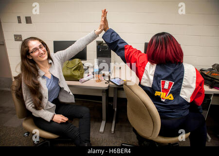 A Caucasian tutor in the learning center of a Santa Ana, CA, community college "high fives" her happy Hispanic student in congratulation for her successful work. Note red dyed hair. Stock Photo
