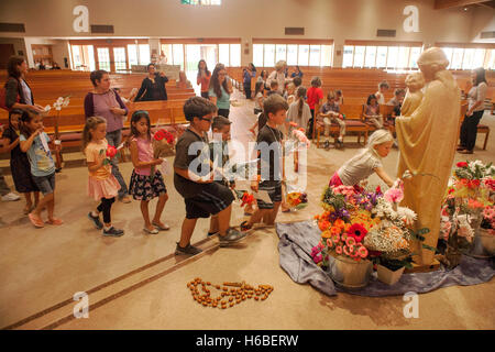 A procession of children place flowers next to a statue of the Virgin Mary during the Crowning of Mary ceremony at  St. Timothy's Catholic Church, Laguna Niguel, CA. The event     refers to special Marian devotions held in the Catholic Church during the m Stock Photo