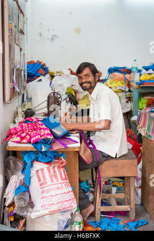 Indian man smiles whilst using a sewing machine in a back street near to the Kapaleeshwarar Temple, Mylapore, Chennai, India Stock Photo