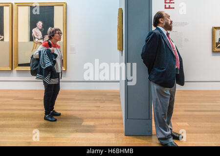 An older female with her audio tour head phones stands in front of a Francis Bacon triptych in a museum  exhibition of his work Stock Photo