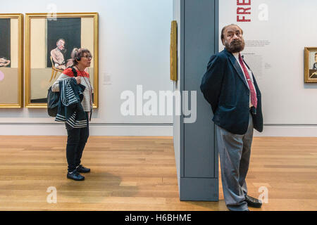 An older female with her audio tour head phones stands in front of a Francis Bacon triptych in a museum  exhibition of his work Stock Photo