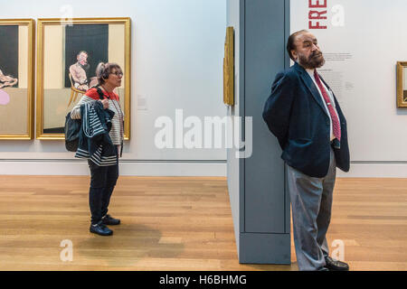 An older female with her audio tour head phones stands in front of a Francis Bacon triptych in a museum  exhibition of his work Stock Photo