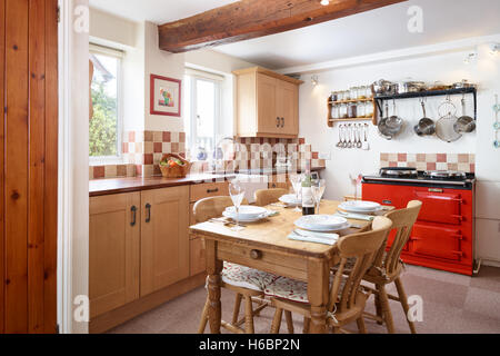 A traditional, fresh country kitchen showing a red Aga, table, units & work surfaces. Gloucestershire, UK Stock Photo