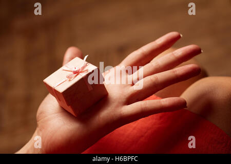 Horizontal side view of an open hand of a woman holding a small pink gift box Stock Photo