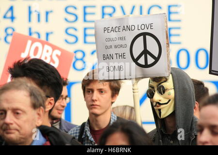 Protesters gather outside of the Ministry of Defense in protest against the UK governments decision to renew its nuclear weapons program Trident. A protester wearing an anonymous mask holds a sign that reads 'Peace and love could free the world, ban the bomb.' Stock Photo