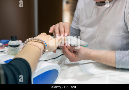 Manicurist master makes nail filing on woman hand closeup, selective focus Stock Photo