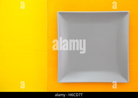 Empty gray ceramic dish on over orange  and yellow wooden table, square dish Stock Photo