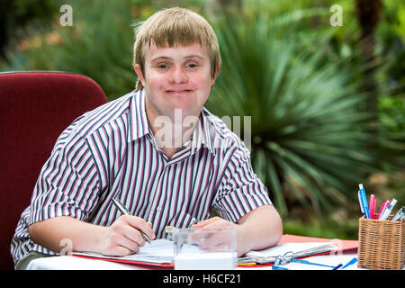 Close up portrait of young male student with down syndrome at study desk outdoors. Stock Photo