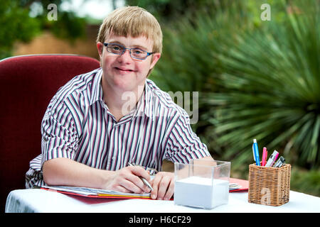 Close up portrait of handicapped student wearing glasses at desk in garden. Stock Photo