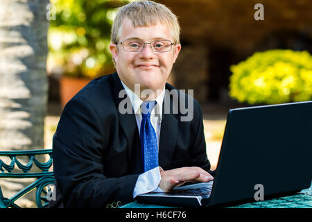 Close up portrait of young businessman with down syndrome doing accounting on laptop outdoors. Stock Photo