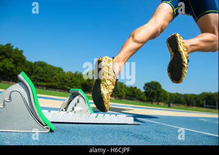 Athlete in gold shoes starting a race from the starting blocks on a blue running track Stock Photo