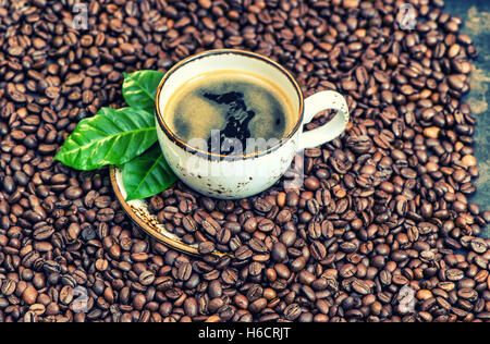 Black coffee with green leaves on coffee beans background. Vintage style toned picture Stock Photo