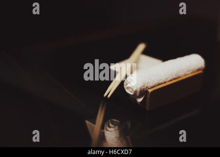 A roll of wet towel, chopsticks for sushi or japanese food and empty plate for sauce  on reflective surface in dark environment Stock Photo