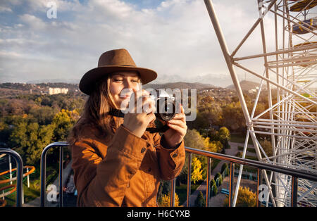 Woman taking picture with vintage camera at the cabin of Ferris wheel in the autumn park at sunset Stock Photo
