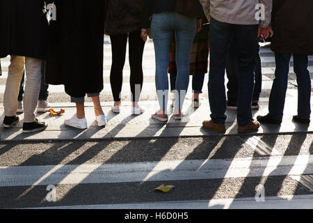 detail of the legs of a crowd of people waiting at the pedestrian crossing Stock Photo