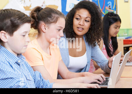 Teacher Helping Female Elementary Pupil In Computer Class Stock Photo
