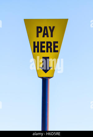 A bright yellow sign with the words Pay Here on and an arrow pointing downwards with a blue sky background. Stock Photo