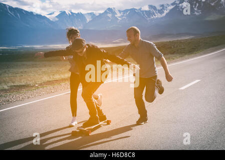 Group of friends run, laugh and having fun. The guy on longboard. Stock Photo