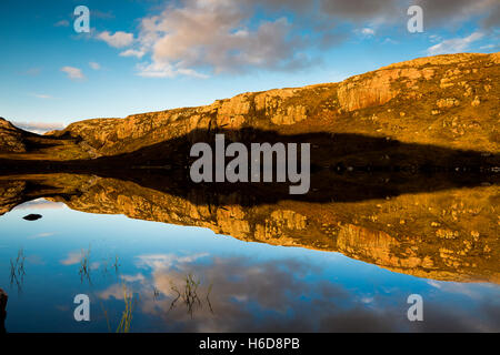 Sunset on rocks reflecting in loch along with a section of the Applecross to Shieldaig road. Stock Photo
