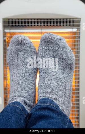 A person wearing cosy thick woolly socks warming cold feet in front of a low energy Halogen room heater to illustrate hygge. England UK Stock Photo