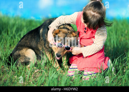 Little girl wears glasses at the big dog on the green lawn Stock Photo