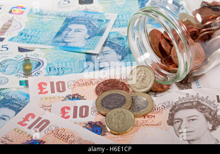Close up of English money polymer five pound notes and coins spilling from a jar finance savings concept England UK United Kingdom GB Great Britain Stock Photo