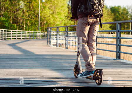 Young man in casual wear on kick scooter in park at sunset Stock Photo