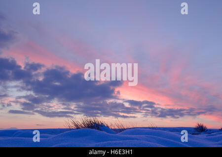 Colourful sky and clouds at daybreak over snow covered mounds in North York Moors national park Stock Photo