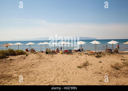 Holiday makers under parasols at the Greek resort of Katelios on the island of Kefalonia with the island of Zante in view Stock Photo
