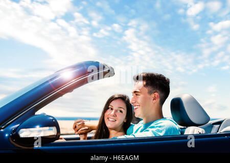 Close up portrait of Happy young couple driving blue convertible along seaside. Stock Photo