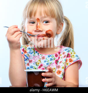 Close up portrait of Cute little girl eating chocolate yogurt at breakfast. Face messy with chocolate and funny face expresstion Stock Photo