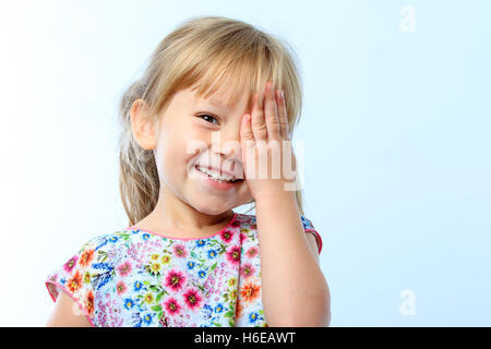 Close up portrait of Cute little girl closing one eye with hand against blue background. Stock Photo