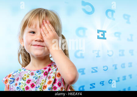 Close up portrait of little girl reading eye chart. Young kid testing one eye on block letter vision chart. Stock Photo