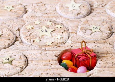 Open window of Advent calendar handmade from old timber. Circular space filled with a small gift and jelly beans. Stock Photo