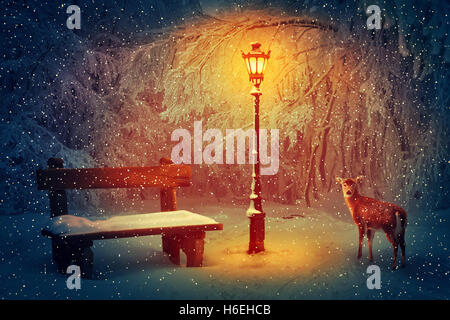 Wooden bench and a glowing lamp in the winter park covered in with snow. Snowing peaceful night scene and a doe looking carefull Stock Photo