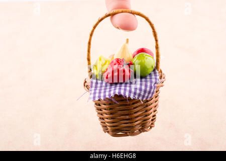 Hand holding a wicker basket with a plastic fruit on a white and wooden background Stock Photo