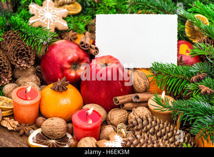 Christmas decoration burning candles and greetings card. Apples, tangerine, nuts, spices and cookies Stock Photo