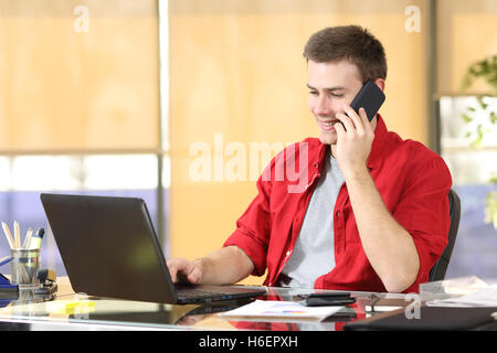 Freelancer working on line and calling by mobile phone sitting in a desktop at office Stock Photo