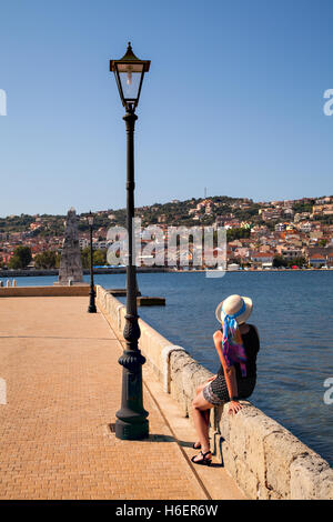 Lady wearing a hat sitting on the Drapano Bridge admiring the view towards the town of Argostoli on the island of Kefalonia Stock Photo