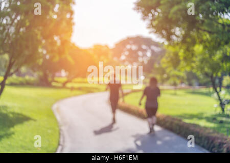 Blurry focus scene of couple walking on the path inside public park with soft orange sunlight in morning. Stock Photo