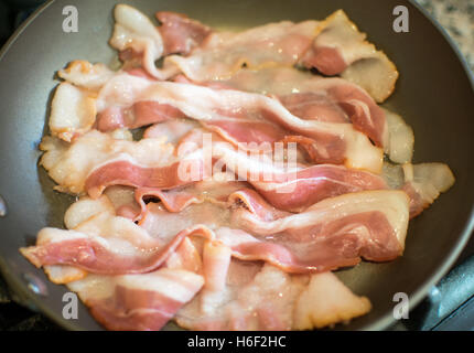 Raw Pork Bacon Strips being Fried in a Teflon Pan Close Up Stock Photo